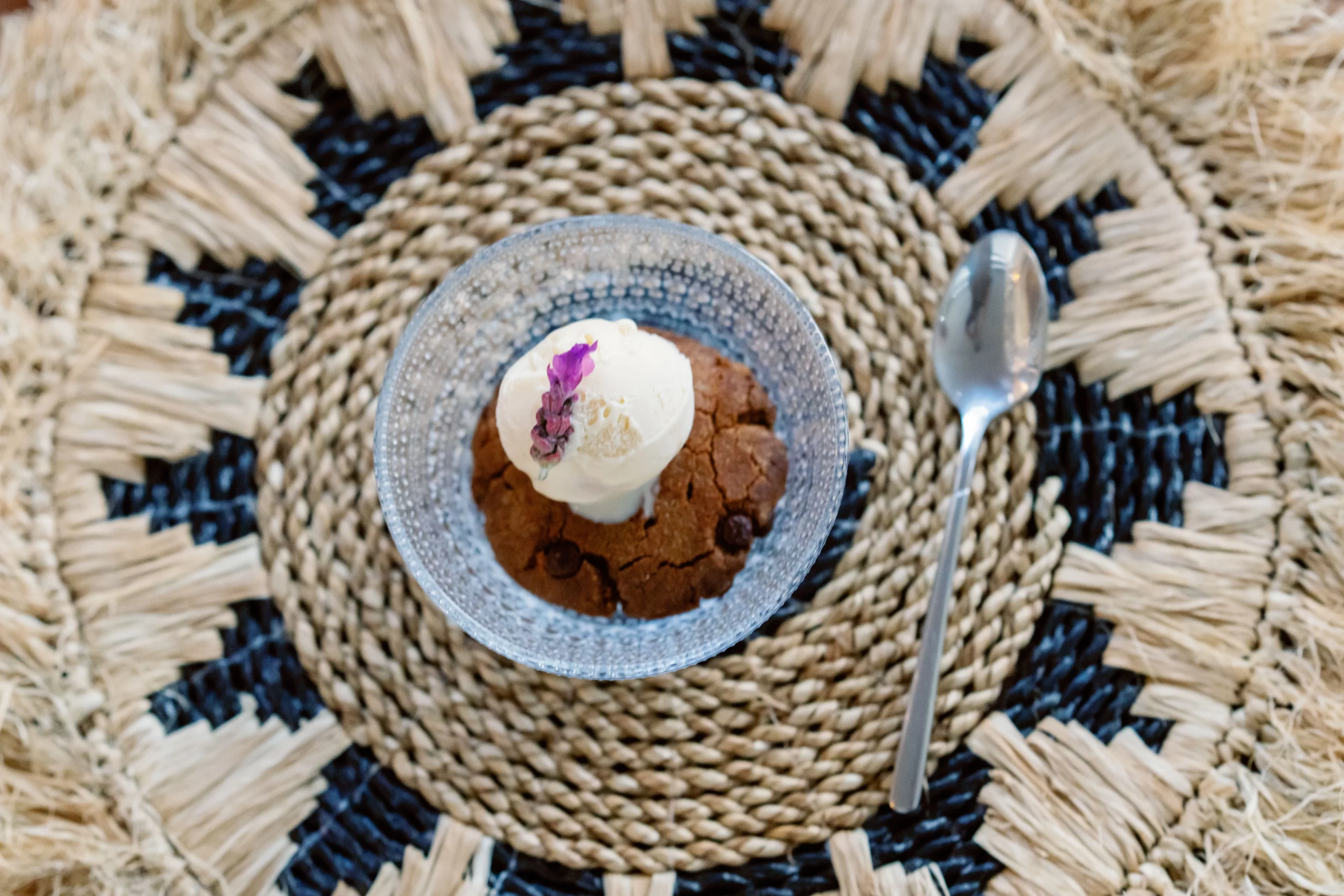 A close-up of a healthy, plant-based chocolate dessert topped with a single fresh raspberry, elegantly served on a rustic woven macramé placemat at the Seeds of Silence wellness retreat in Algarve, Portugal.